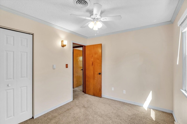 unfurnished bedroom featuring ceiling fan, crown molding, a closet, and light carpet