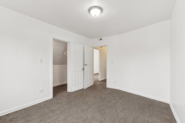 unfurnished bedroom featuring a walk in closet, a closet, and dark colored carpet