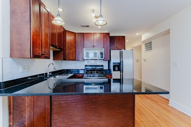 kitchen featuring a sink, gas range, fridge with ice dispenser, stainless steel microwave, and a peninsula