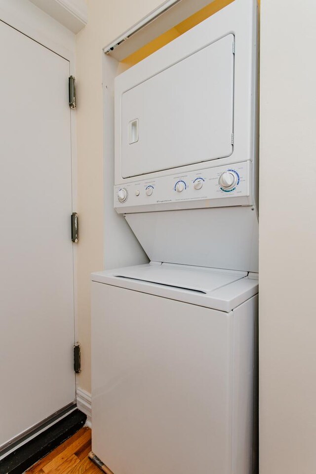 laundry room featuring stacked washer / drying machine, wood finished floors, and laundry area