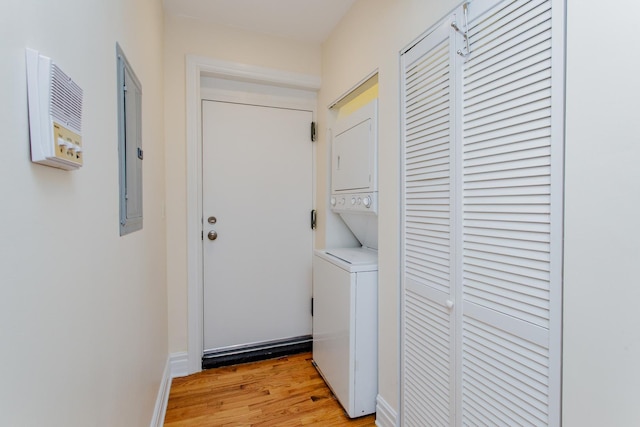laundry area with stacked washer / drying machine, electric panel, light wood-style flooring, and laundry area