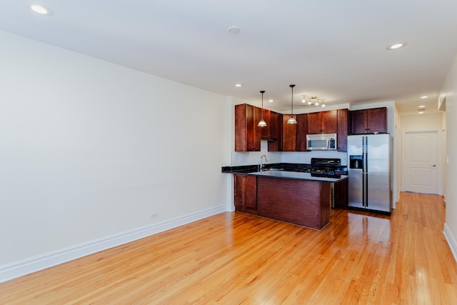 kitchen featuring decorative light fixtures, kitchen peninsula, sink, light hardwood / wood-style flooring, and stainless steel appliances