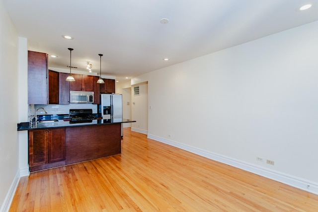 kitchen with a sink, stainless steel microwave, dark countertops, fridge with ice dispenser, and range with gas stovetop
