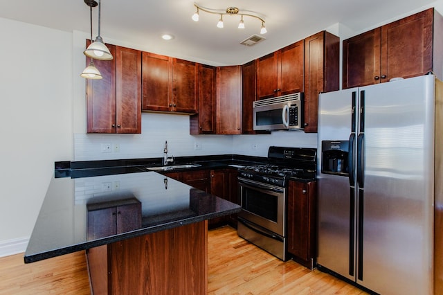 kitchen featuring stainless steel appliances, a sink, light wood-type flooring, visible vents, and decorative light fixtures