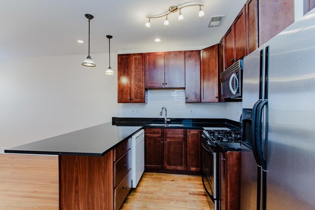 kitchen featuring stainless steel appliances, dark countertops, visible vents, a sink, and light wood-style floors