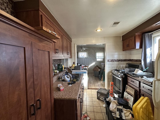 kitchen featuring ceiling fan, sink, light tile patterned floors, and stainless steel gas range oven