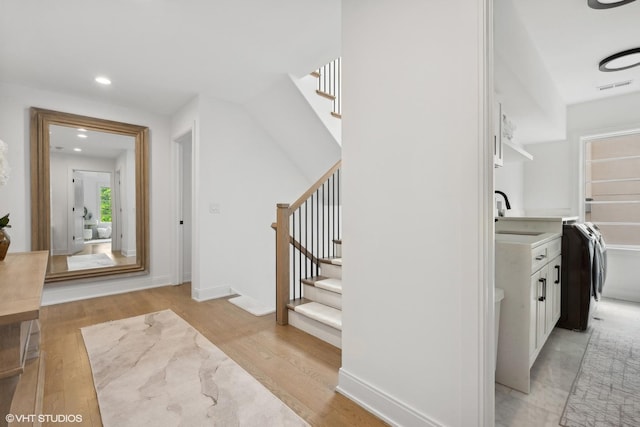 stairs with washer / dryer, hardwood / wood-style floors, and sink