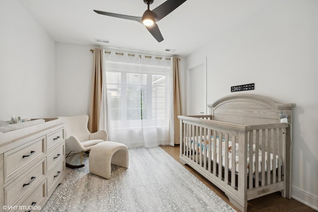 bedroom featuring ceiling fan, wood-type flooring, and a crib