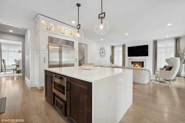 kitchen with dark brown cabinets, white cabinets, built in appliances, pendant lighting, and light hardwood / wood-style flooring