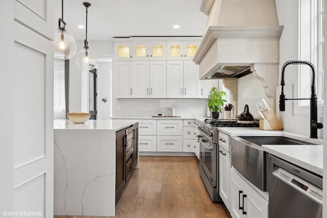 kitchen with decorative light fixtures, white cabinetry, light stone countertops, appliances with stainless steel finishes, and custom range hood