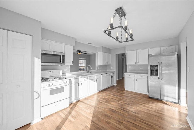 kitchen with white cabinetry, appliances with stainless steel finishes, wood-type flooring, ceiling fan with notable chandelier, and sink