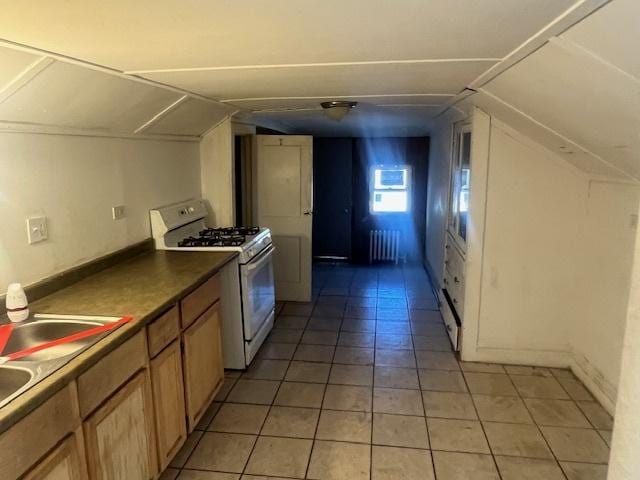 kitchen with vaulted ceiling, sink, white range with gas cooktop, radiator, and light tile patterned floors