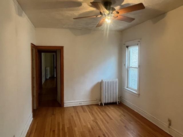 empty room featuring ceiling fan, radiator heating unit, and light hardwood / wood-style floors