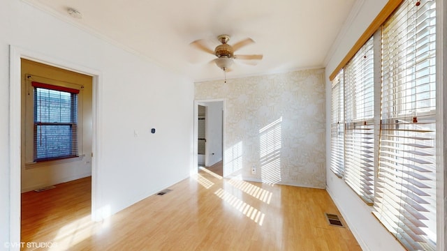 unfurnished room featuring light hardwood / wood-style floors, a wealth of natural light, crown molding, and ceiling fan