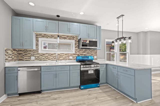 kitchen with decorative light fixtures, kitchen peninsula, sink, light hardwood / wood-style flooring, and stainless steel appliances