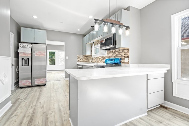 kitchen featuring backsplash, pendant lighting, light hardwood / wood-style floors, kitchen peninsula, and appliances with stainless steel finishes