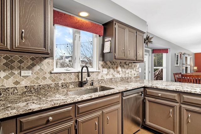 kitchen with kitchen peninsula, backsplash, light stone countertops, stainless steel dishwasher, and sink