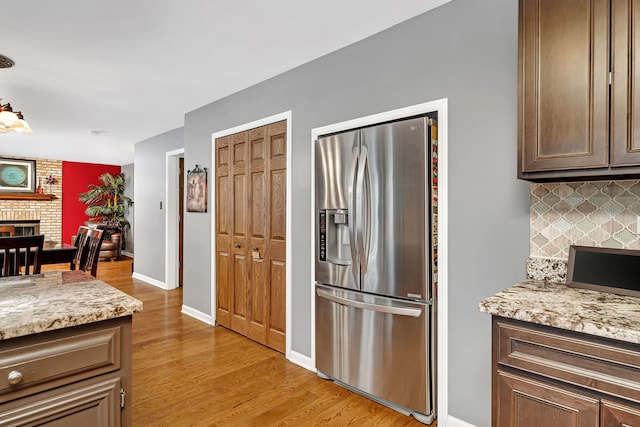 kitchen with backsplash, a fireplace, light hardwood / wood-style floors, stainless steel refrigerator with ice dispenser, and light stone counters