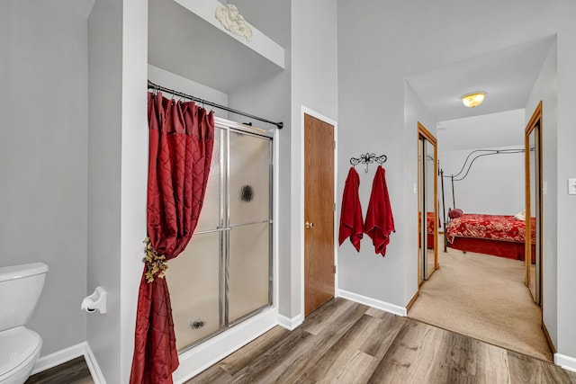 bathroom with toilet, a shower with door, and hardwood / wood-style floors