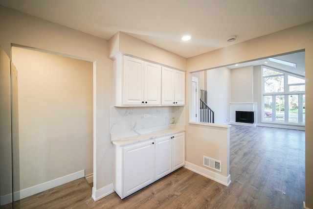 kitchen with vaulted ceiling, dark hardwood / wood-style floors, white cabinets, backsplash, and light stone countertops