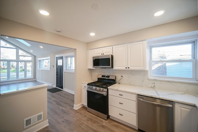 kitchen with stainless steel appliances, white cabinetry, light stone counters, and decorative backsplash