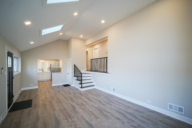 unfurnished living room featuring sink, a skylight, light hardwood / wood-style floors, and high vaulted ceiling