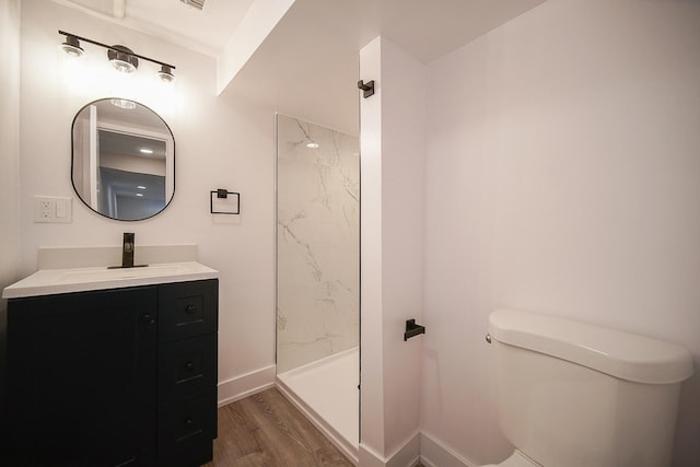 bathroom featuring a tile shower, hardwood / wood-style floors, vanity, and toilet