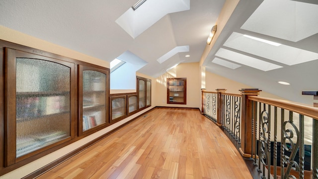 additional living space with lofted ceiling with skylight and light wood-type flooring