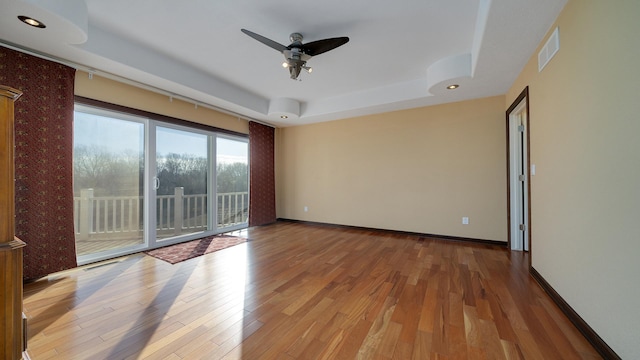 empty room with a tray ceiling, light hardwood / wood-style flooring, and ceiling fan