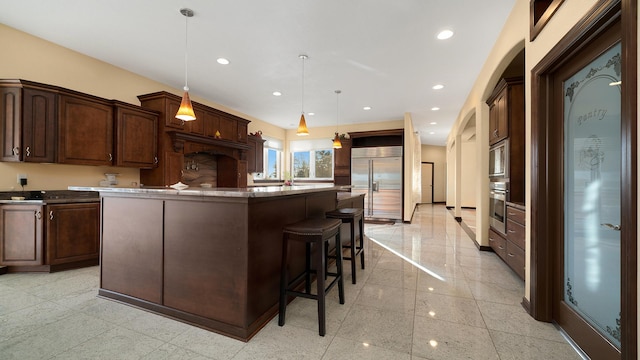 kitchen with a kitchen breakfast bar, a kitchen island, pendant lighting, and built in appliances