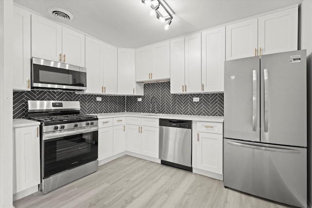 kitchen featuring light wood-type flooring, appliances with stainless steel finishes, decorative backsplash, and white cabinetry