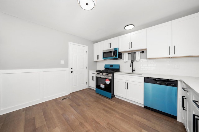 kitchen featuring sink, appliances with stainless steel finishes, white cabinetry, wood-type flooring, and decorative backsplash