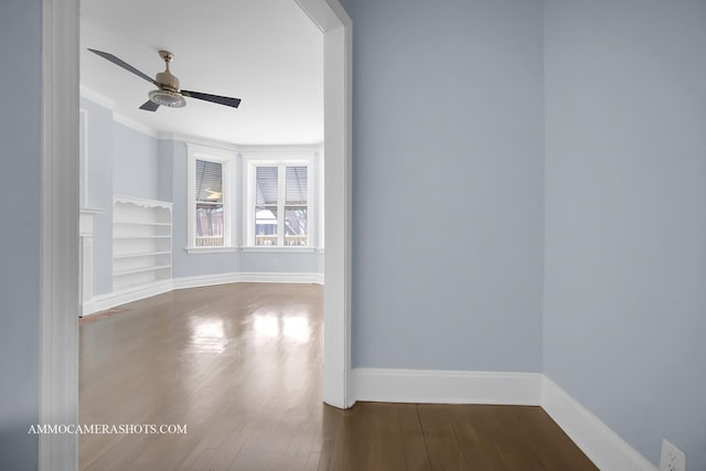 spare room with ceiling fan, built in shelves, dark hardwood / wood-style flooring, and crown molding