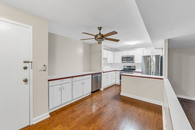 kitchen with white cabinets, a textured ceiling, appliances with stainless steel finishes, and hardwood / wood-style floors