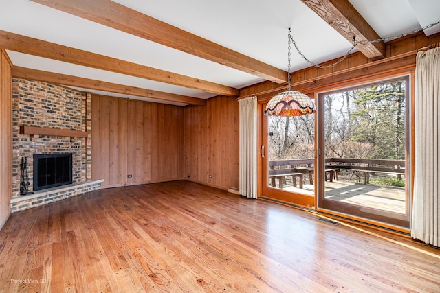 unfurnished living room with a brick fireplace, beam ceiling, hardwood / wood-style floors, and wooden walls