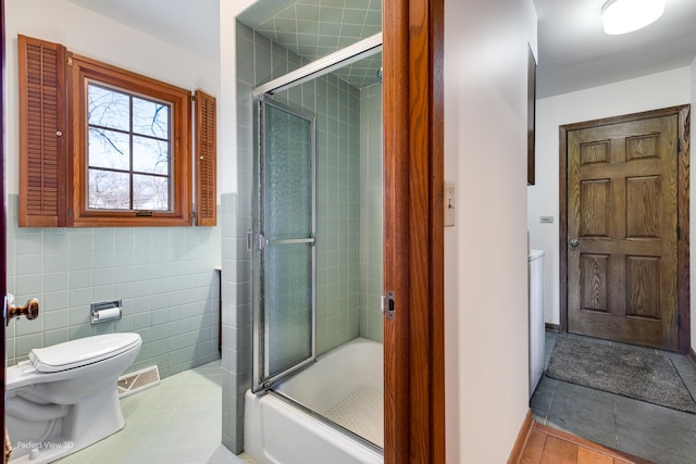 bathroom with toilet, tile walls, shower / bath combination with glass door, and tile patterned flooring