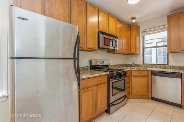 kitchen with light stone counters, sink, light tile patterned floors, and stainless steel appliances