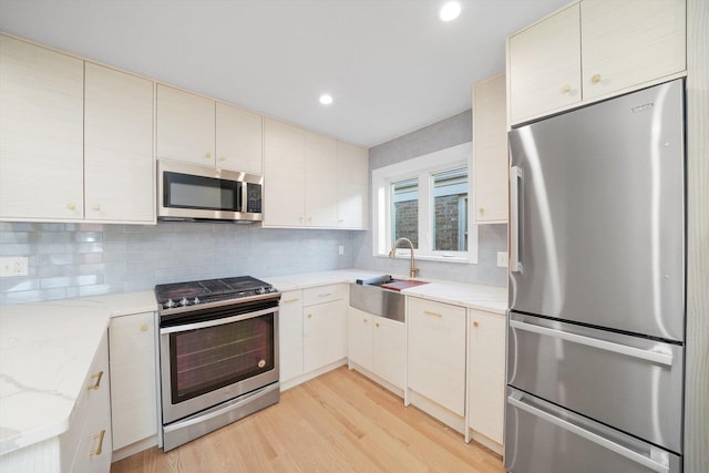 kitchen featuring appliances with stainless steel finishes, sink, backsplash, light stone counters, and light hardwood / wood-style flooring