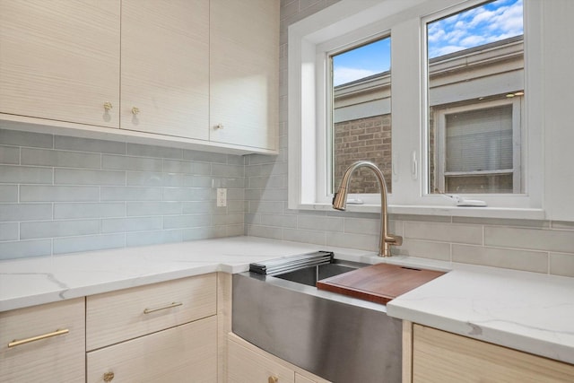 kitchen featuring light brown cabinetry, light stone counters, decorative backsplash, and sink