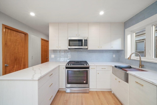 kitchen featuring tasteful backsplash, appliances with stainless steel finishes, kitchen peninsula, and light hardwood / wood-style floors