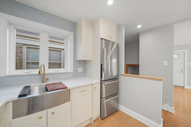 kitchen featuring sink, tasteful backsplash, stainless steel refrigerator, light stone countertops, and light hardwood / wood-style floors