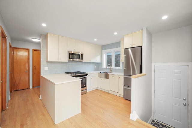 kitchen with sink, tasteful backsplash, kitchen peninsula, stainless steel appliances, and light hardwood / wood-style floors