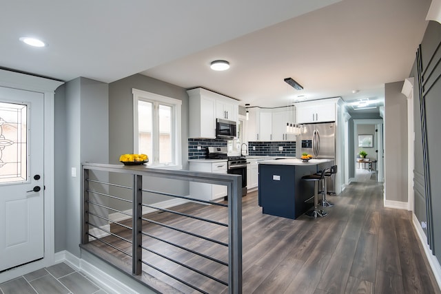 kitchen with white cabinetry, stainless steel appliances, backsplash, a kitchen island, and a breakfast bar