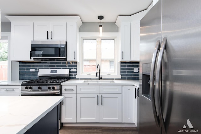 kitchen with appliances with stainless steel finishes, a healthy amount of sunlight, decorative light fixtures, white cabinets, and sink