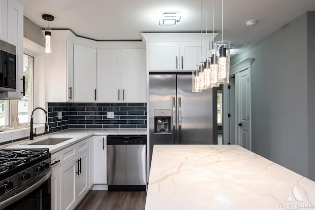 kitchen featuring light stone countertops, appliances with stainless steel finishes, white cabinetry, and decorative light fixtures