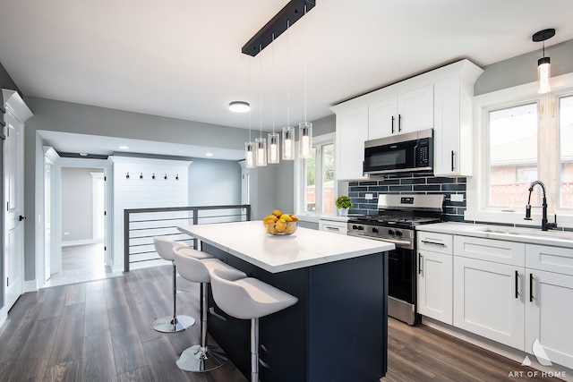 kitchen featuring decorative light fixtures, a kitchen island, sink, white cabinetry, and stainless steel appliances