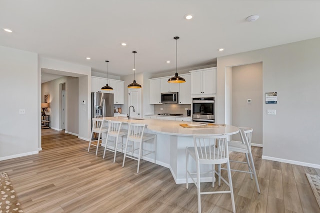 kitchen featuring a large island with sink, decorative light fixtures, a kitchen bar, white cabinetry, and stainless steel appliances