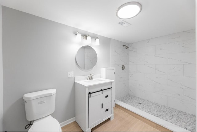 bathroom featuring toilet, vanity, hardwood / wood-style flooring, and a tile shower