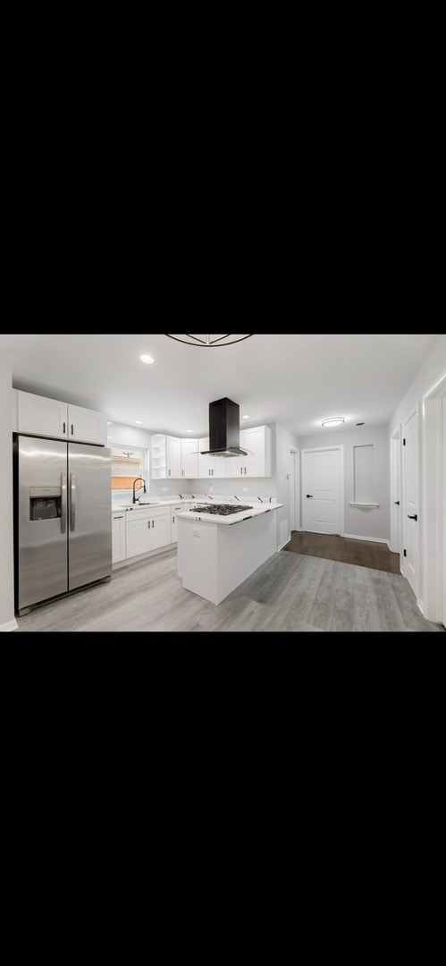 kitchen with light hardwood / wood-style floors, kitchen peninsula, stainless steel refrigerator with ice dispenser, white cabinetry, and island range hood