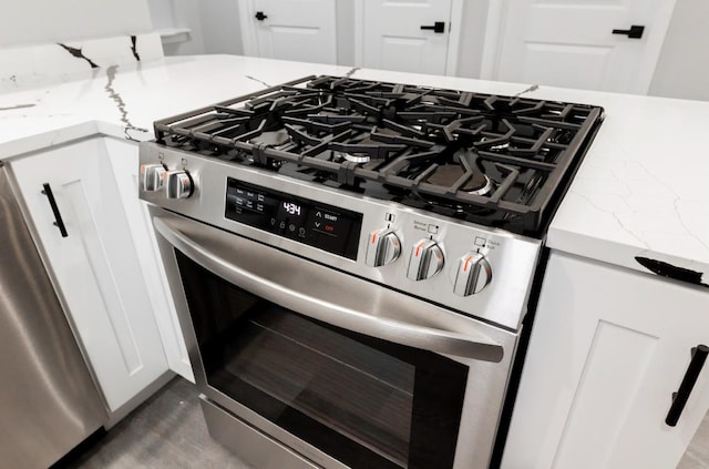 details featuring light stone counters, white cabinets, and stainless steel range with gas cooktop